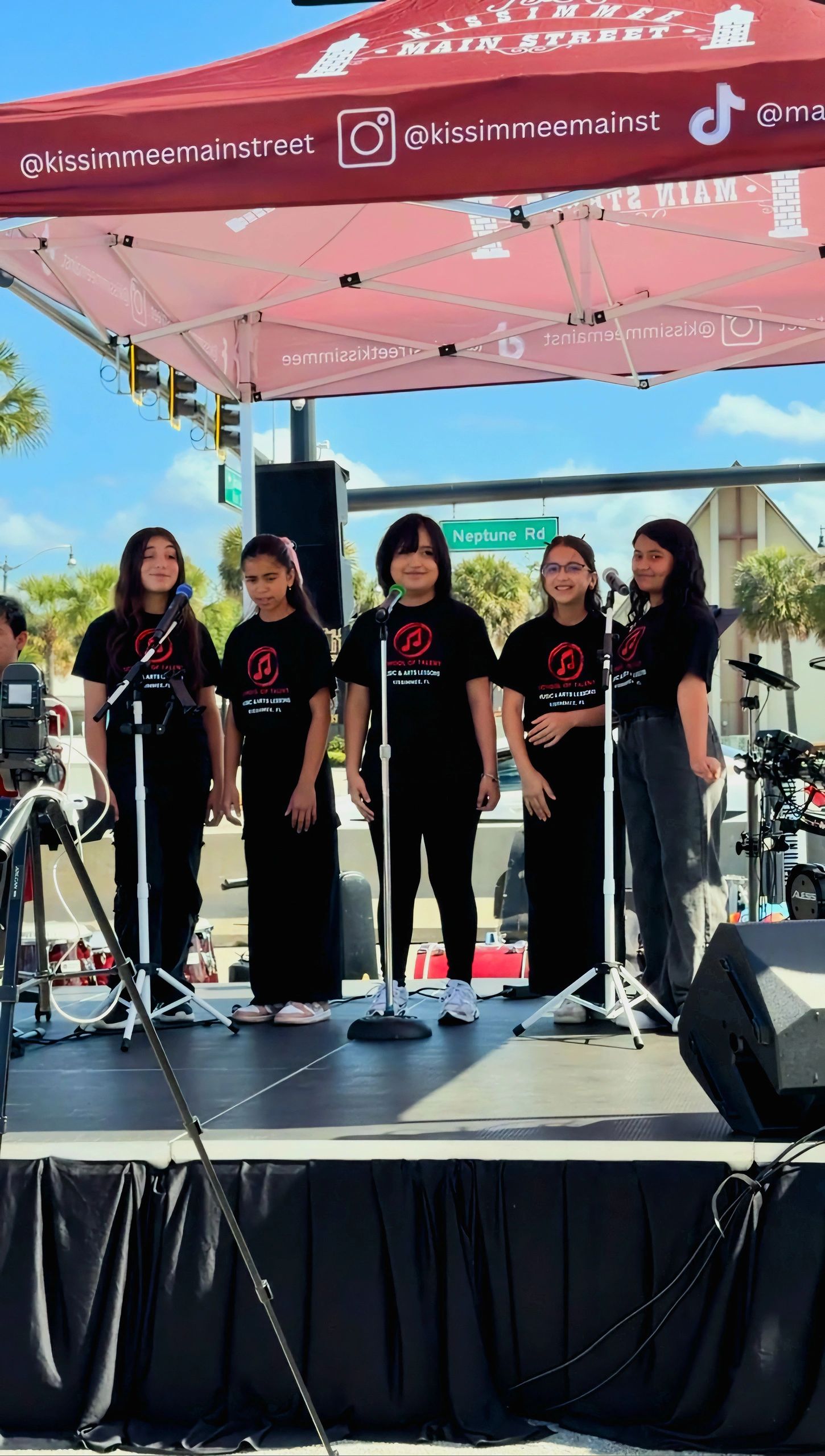 Five School of Talent students at microphones during Kissimmee’s Hop On Downtown event, in a different photograph from the article images