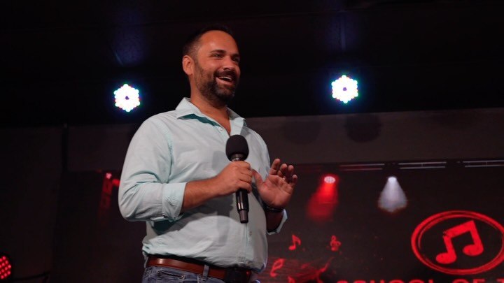 A parent speaking into a microphone on the concert stage